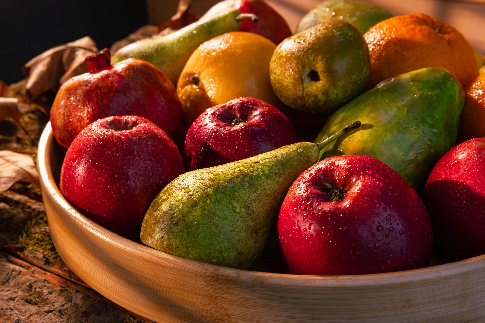 Close-Up Shot of Fresh Fruits in Wooden Basket with Water Droplets, Autumn leaves and Sunbeam Over Basket and Background - Stock Photo